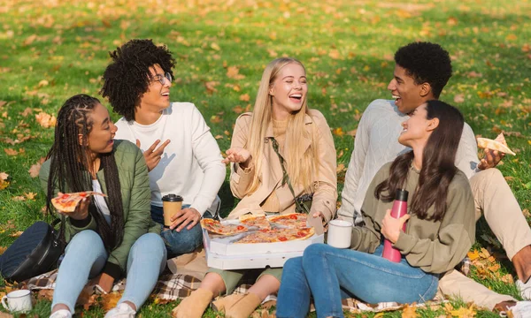 Alunos alegres compartilhando suas histórias enquanto comem pizza no parque — Fotografia de Stock