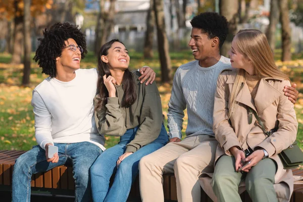 Смешанные расовые подростковые пары сидят на скамейке в общественном парке — стоковое фото