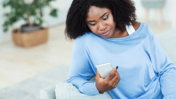 Black lady checking mobile phone sitting on the couch