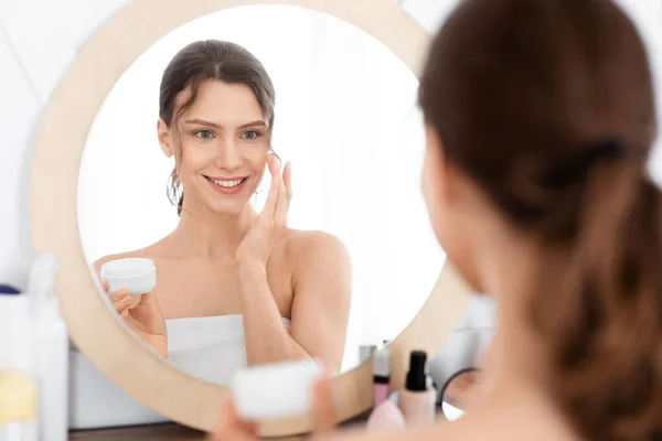 Gut aussehende junge Dame benutzt Gesichtscreme — Stockfoto