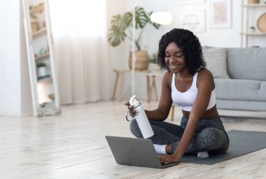 Evde dizüstü bilgisayar kullanarak egzersiz yapan Afrikalı güzel bir bayan.