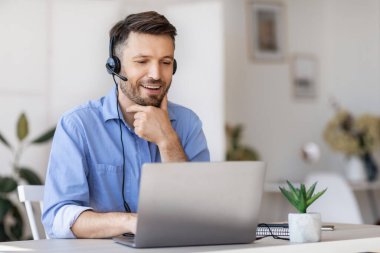 İş Eğitimi. Kulaklık takmış yakışıklı bir işadamı laptopta ofiste Webinar izliyor.