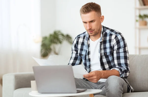 Ein aufgeweckter junger Mann sitzt am Schreibtisch und schaut sich Dokumente an — Stockfoto