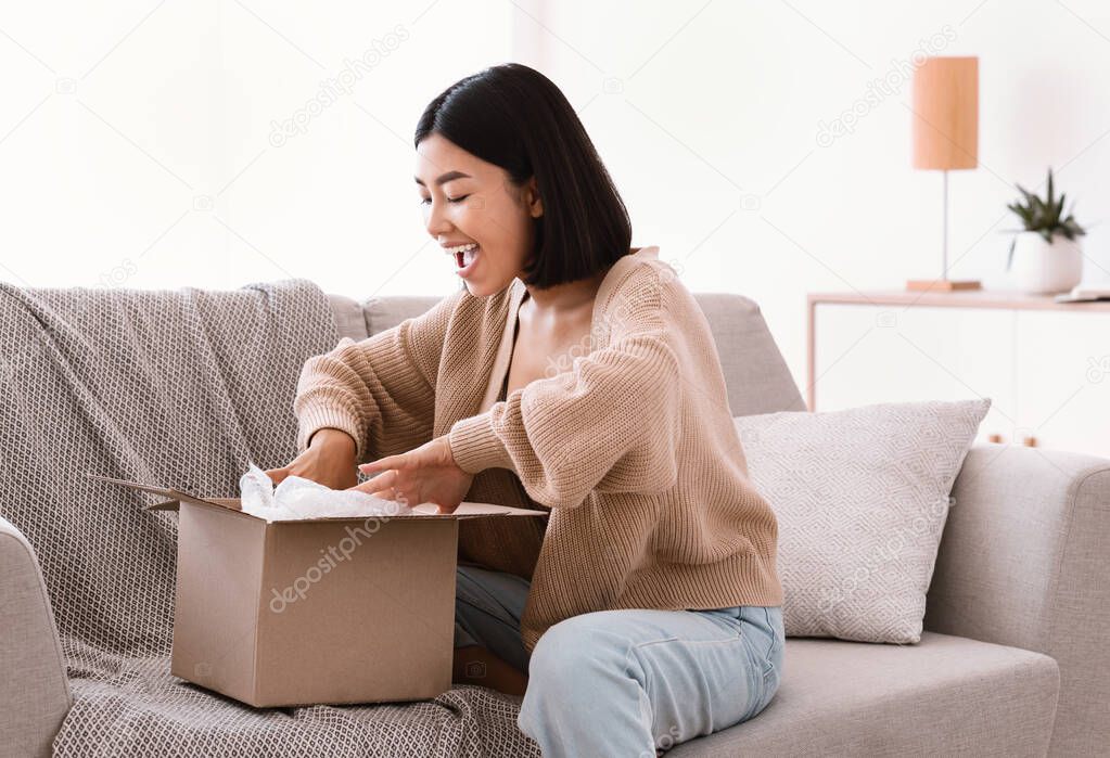 Happy asian woman unpacking parcel after online shopping