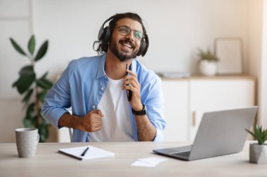 Neşeli Hintli bağımsız adam çalışırken şarkı söylüyor ve kulaklıkla müzik dinliyor.