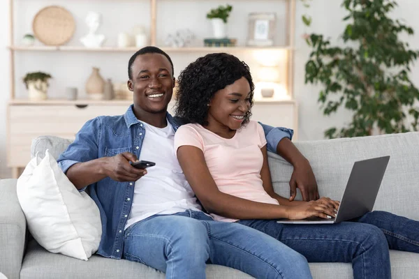 Genç Afro-Amerikan çift televizyon izliyor ve dizüstü bilgisayar kullanıyorlar. — Stok fotoğraf