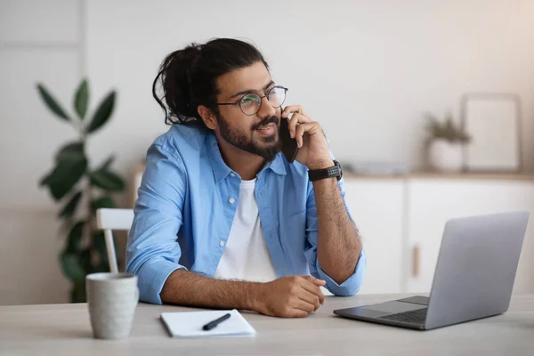 Millennial Indiase man praten op mobiele telefoon en het gebruik van laptop op het thuiskantoor — Stockfoto