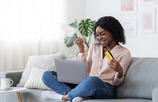 Gioiosa donna nera che festeggia il successo dello shopping su Internet con computer portatile e carta di credito — Foto Stock