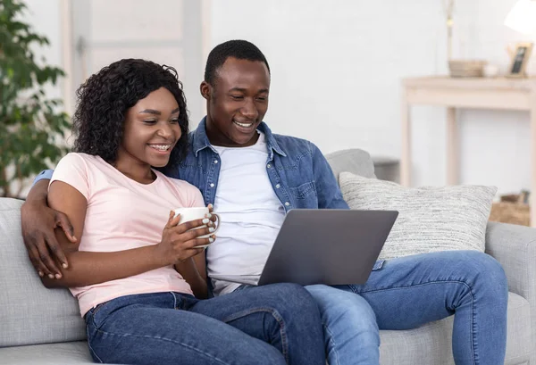 Joyful black couple watching movie online, using laptop