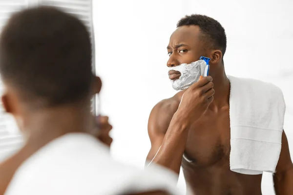 Africano americano hombre afeitado cara de pie sin camisa en moderno cuarto de baño — Foto de Stock