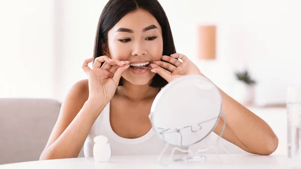 Молодая азиатка с зубной нитью, смотрящая в зеркало — стоковое фото