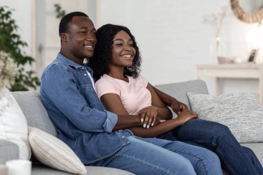 Neşeli Afrikalı çift evdeki kanepede sarılıyor.