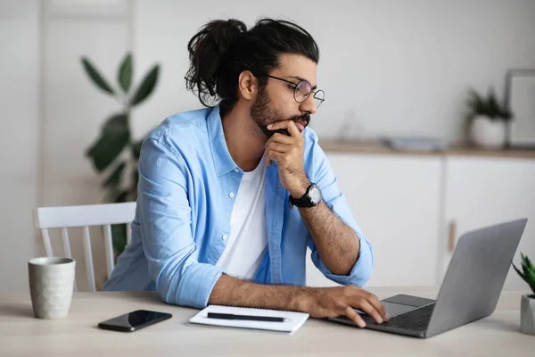 Nachdenkliche indische Freelancer arbeiten mit Laptop im Home Office, Blick auf den Bildschirm — Stockfoto