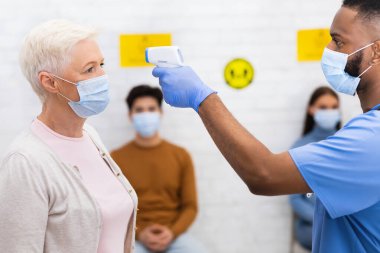 Doktor, içeride randevudan önce yaşlı bayan hasta için sıcaklık ölçümü yapıyor.
