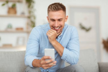 Evde cep telefonu kullanan gülümseyen adamın yakın plan fotoğrafı.
