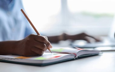 Ofiste dizüstü bilgisayarla çalışırken not alan tanınmamış Afrikalı kadın sekreter.
