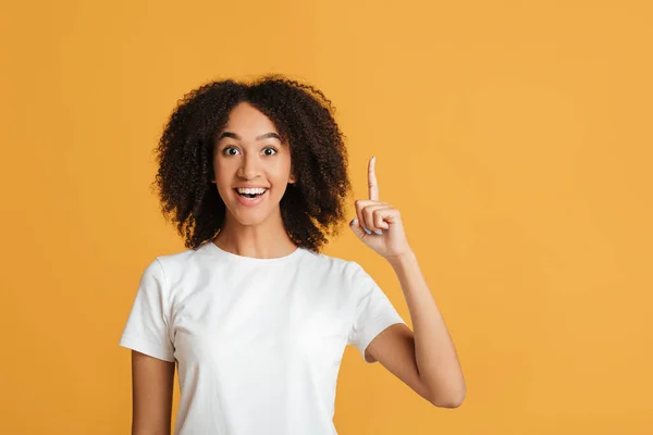 Gran idea y buen humor. Joven mujer afroamericana inteligente lleva casual con la boca abierta señalando el dedo hacia arriba en el espacio libre y tiene un plan exitoso — Foto de Stock