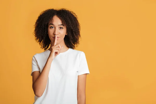 Secreto para todos. Millennial afroamericana mujer con expresión seria muestra signo de silencio, poner el dedo en sus labios aislados sobre fondo naranja, filmación de estudio — Foto de Stock