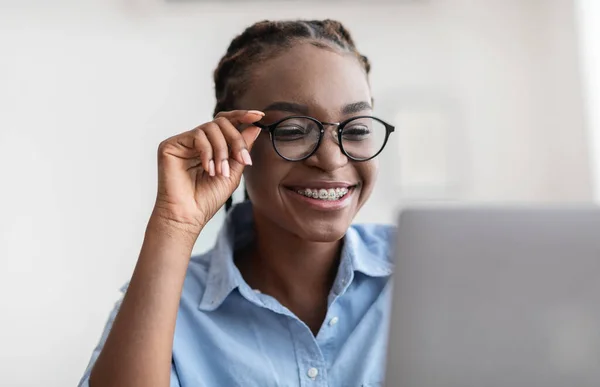 Especialista Joven. Mujer africana con anteojos y aparatos ortopédicos usando portátil en la oficina —  Fotos de Stock