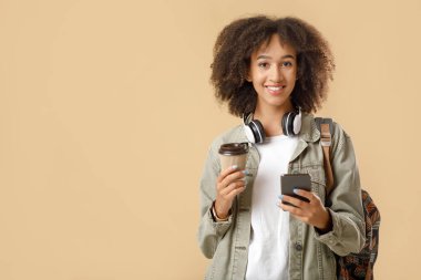 Modern öğrenci hipster dersten sonra kahve molası veriyor. Kablosuz kulaklıkları, sırt çantaları ve akıllı telefonuyla kahve yazan neşeli Afro-Amerikalı kadın.