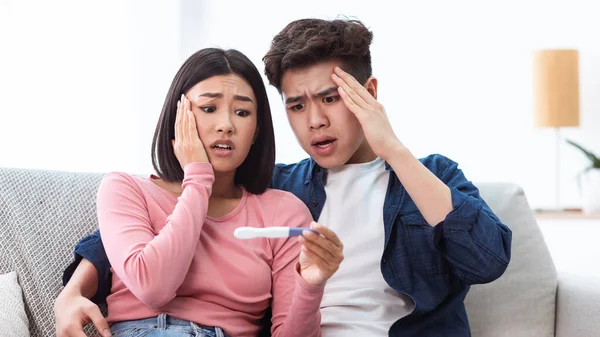 Nešťastný mladý asijské pár držení pozitivní těhotenský test vnitřní, panorama — Stock fotografie