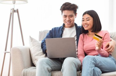 İnternette dizüstü bilgisayarı olan Asyalı çift kredi kartını içeride tutuyor.