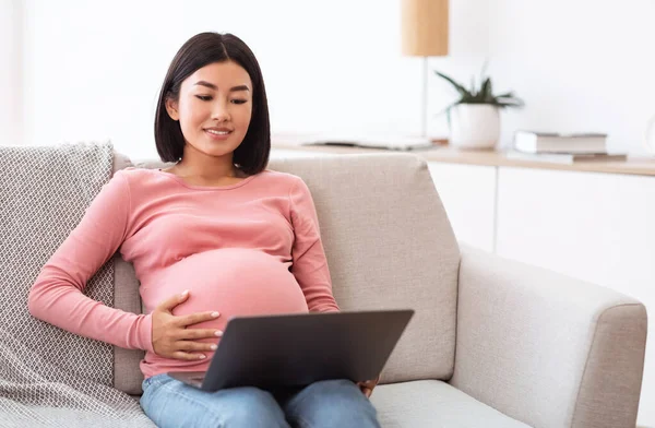 Aziatisch zwanger vrouw met behulp van laptop zitten op bank thuis — Stockfoto