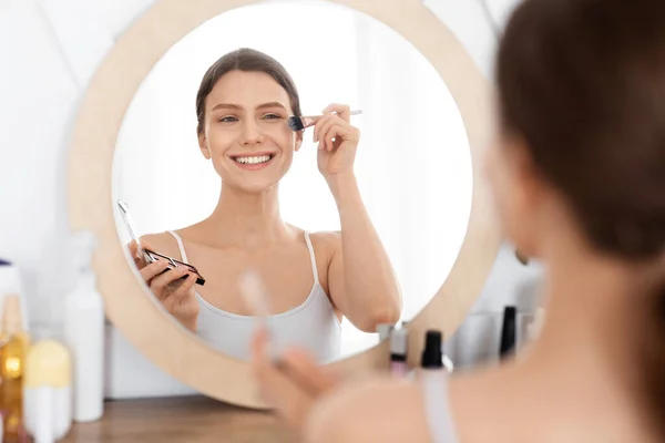 Sonriente joven atractiva haciendo maquillaje antes de salir —  Fotos de Stock