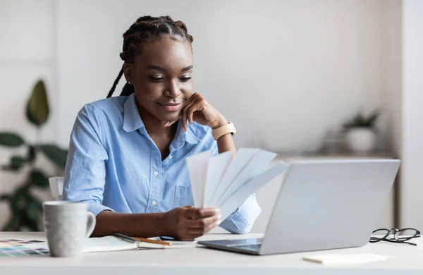 Joven diseñadora negra sosteniendo y mirando muestras de color en la oficina —  Fotos de Stock