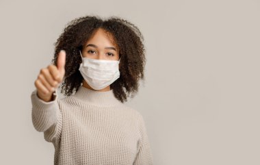 Güzel, onaylayın. Milenyum dostu Afrika kökenli koruyucu maskeli Amerikalı kadın baş parmak işareti gösteriyor.