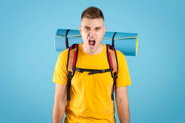 Rozzlobený mladý cestovatel s batohem křičí na modrém pozadí studia — Stock fotografie