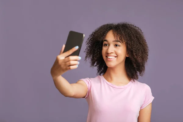 현대 기술, 모바일 앱, 그리고 패션 블로그를 위한 셀피. 아프리카계 미국인 여성이 보라색 배경에 고립 된 스마트폰으로 사진을 찍고 있습니다 — 스톡 사진