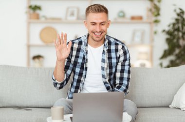 Mutlu adam video görüşmesi ve el sallama için dizüstü bilgisayar kullanıyor.
