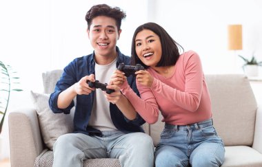 Neşeli Asyalı çift evde oturmuş video oyunu oynuyor.