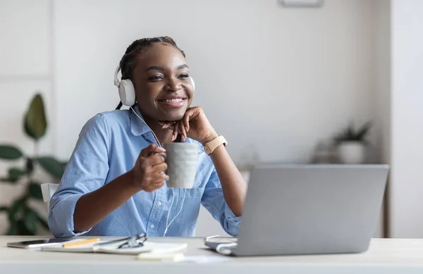 Ονειρεμένη δουλειά. Χαρούμενη μαύρη γυναίκα επιχειρηματίας ακούγοντας μουσική και πίνοντας καφέ στο χώρο εργασίας — Φωτογραφία Αρχείου