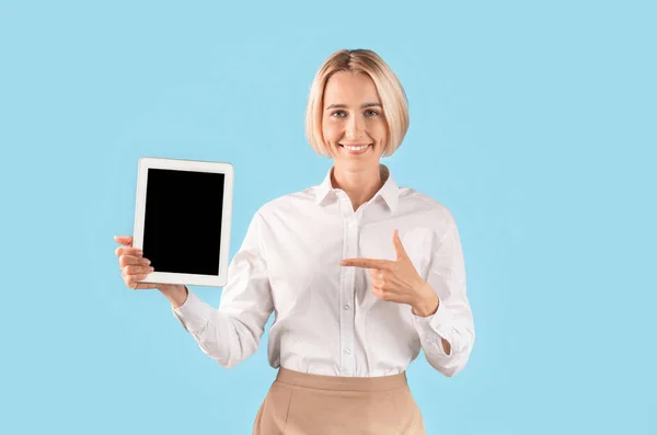 Pozitivní podnikatelka ukazuje na tablet počítač s prázdnou obrazovkou pro design webových stránek přes modré studio pozadí — Stock fotografie