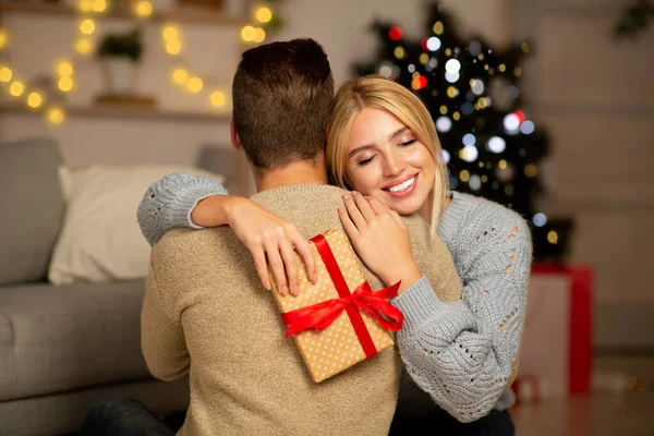 Благодарная женщина держит рождественский подарок и обнимает своего мужчину — стоковое фото