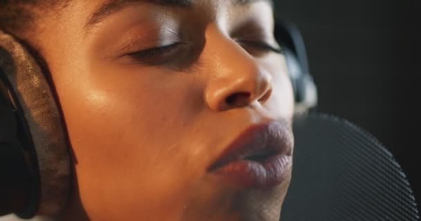 Primer plano de la emotiva dama negra grabando una nueva canción, cantando con los ojos cerrados al micrófono en el estudio de grabación de sonido — Vídeo de stock