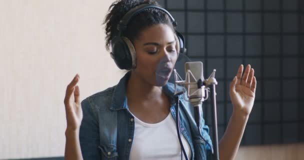 Jonge zwarte vrouw neemt nieuw nummer op in moderne geluidsstudio, zingt in microfoon en danst — Stockvideo