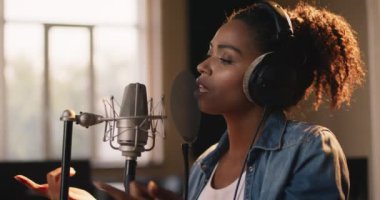 Müzik prodüksiyonu. Afrika kökenli Amerikalı kadın şarkıcının portresi. Ses kayıt stüdyosunda mikrofona şarkı söylüyor.