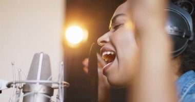 Yetenekli Afrikalı Amerikalı kadın mikrofonda duygusal bir şekilde şarkı söylüyor. Ses kayıt stüdyosunda, yan görüntüde şarkı söylüyor.