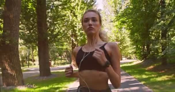 Millennial kvinna tränar springa träning i parken, lyssna på motiverande musik — Stockvideo