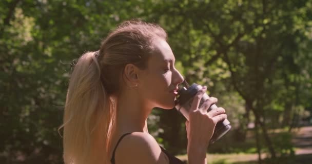 Відстеження зйомок молодої спортивної дівчини, що п'є воду на відкритому повітрі та сміється — стокове відео