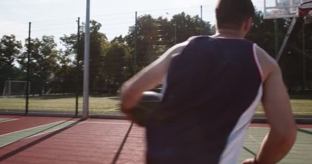 Joven lanzando pelota en el aro, jugando solo en la cancha de baloncesto — Vídeo de stock