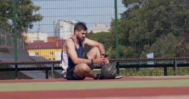 Genç sakallı adam dışarıda basketbol sahasında akıllı telefondan mesaj atıyor.
