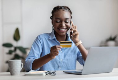 Cep telefonu ödemeleri. İş kadını kredi kartını tutuyor ve ofiste cep telefonuyla konuşuyor.