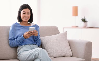 Gülümseyen kadın evinde akıllı telefon kullanıyor.