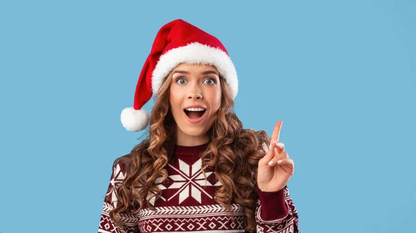 Ritratto di giovane donna eccitata in cappello di Babbo Natale che punta verso l'alto su sfondo blu studio, panorama — Foto Stock