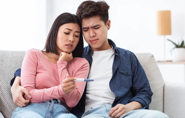 伤心的亚洲夫妇抱着负性怀孕测试坐在家里 — 图库照片
