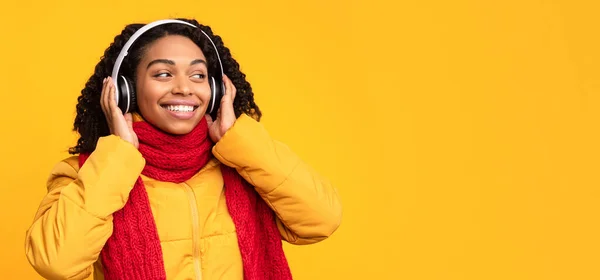 黄色の背景の上にイヤホンで音楽を聴くアフリカの女性 — ストック写真